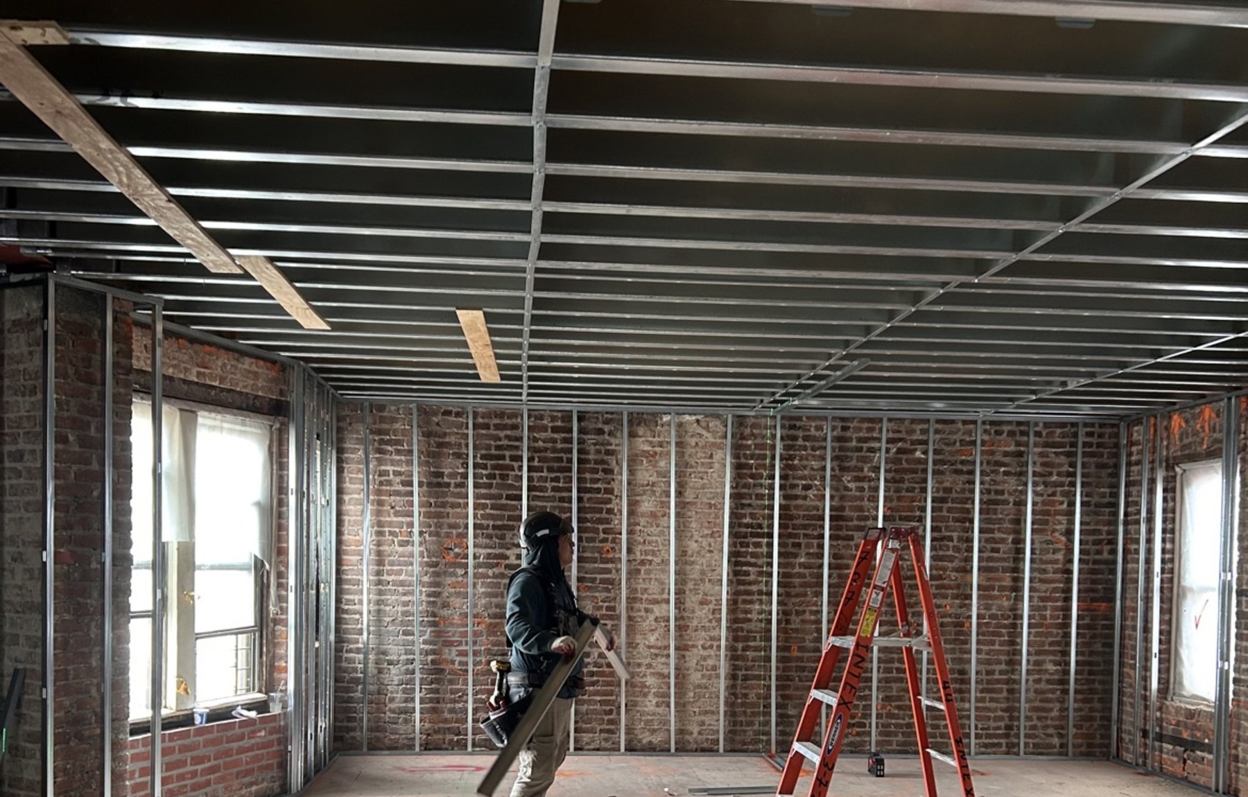 J&A Pro Builders crew framing a large interior space with metal studs and exposed brick