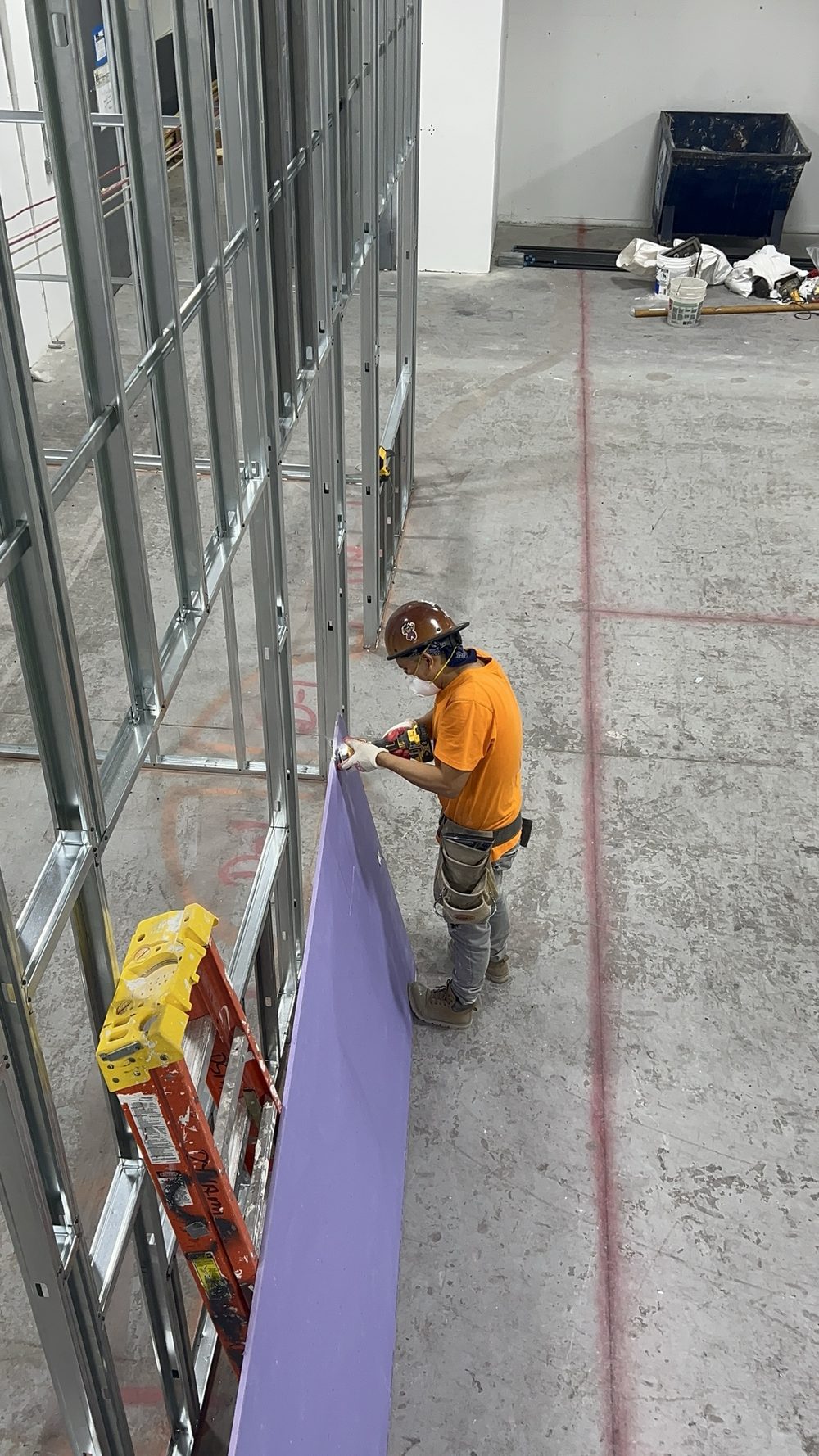 Worker cutting and hanging a sheet of drywall on a metal stud wall