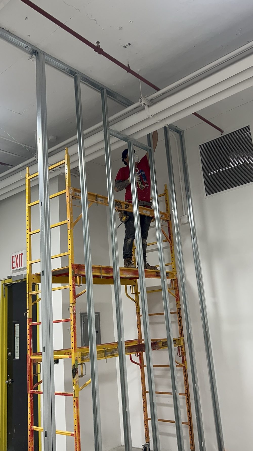 Worker on a scaffold building a tall metal stud framed wall