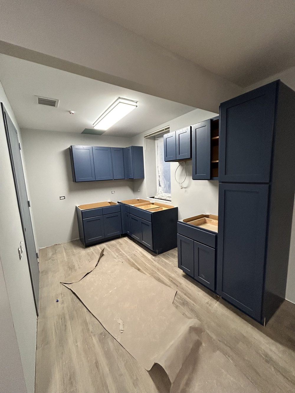 Kitchen with newly installed navy blue shaker cabinets and light wood flooring