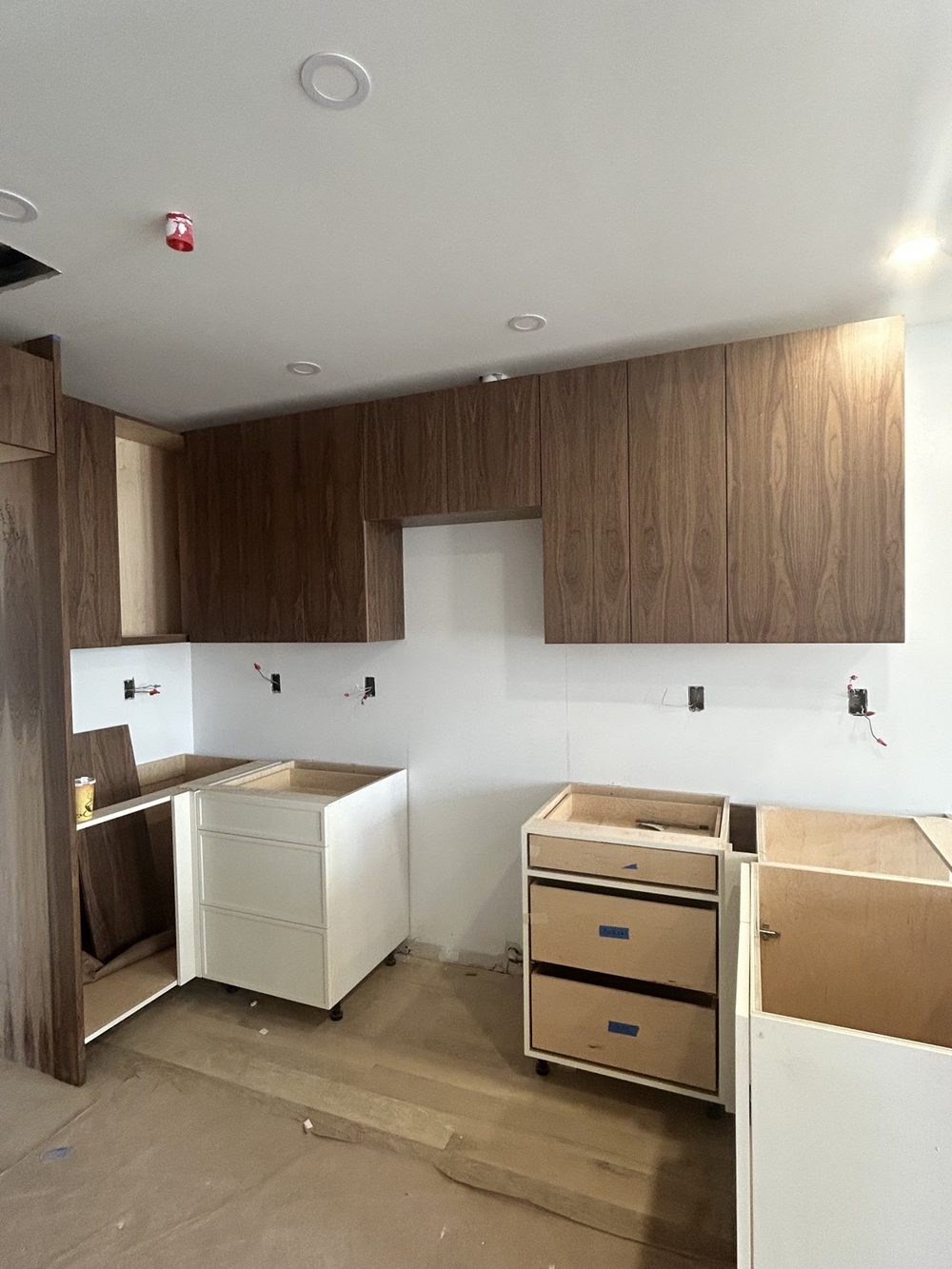 Walnut wood wall cabinets installed above white base cabinets in a new kitchen